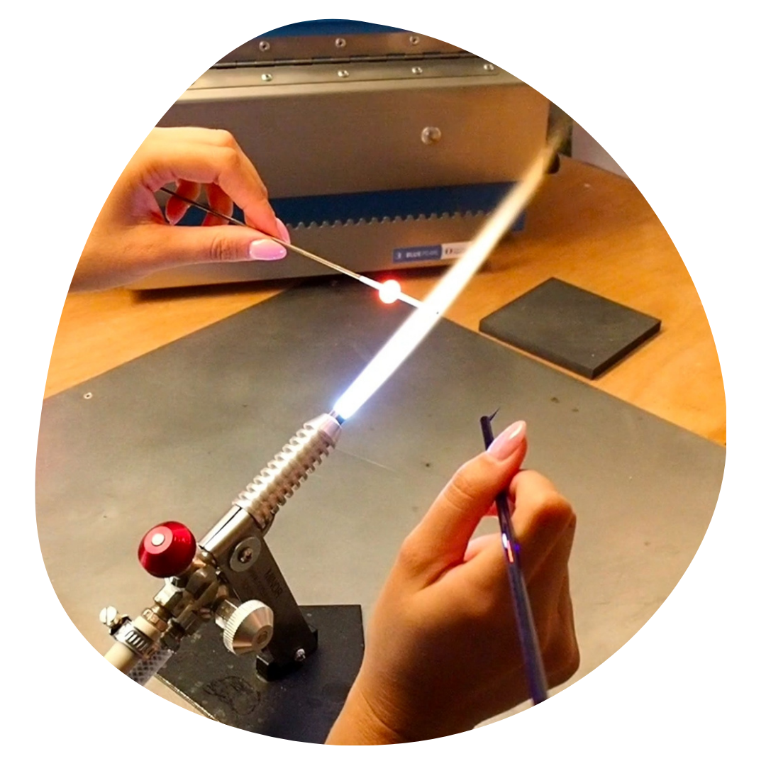 Lola façonnant des perles en verre grâce à la technique du filage de verre au chalumeau - May Atoria